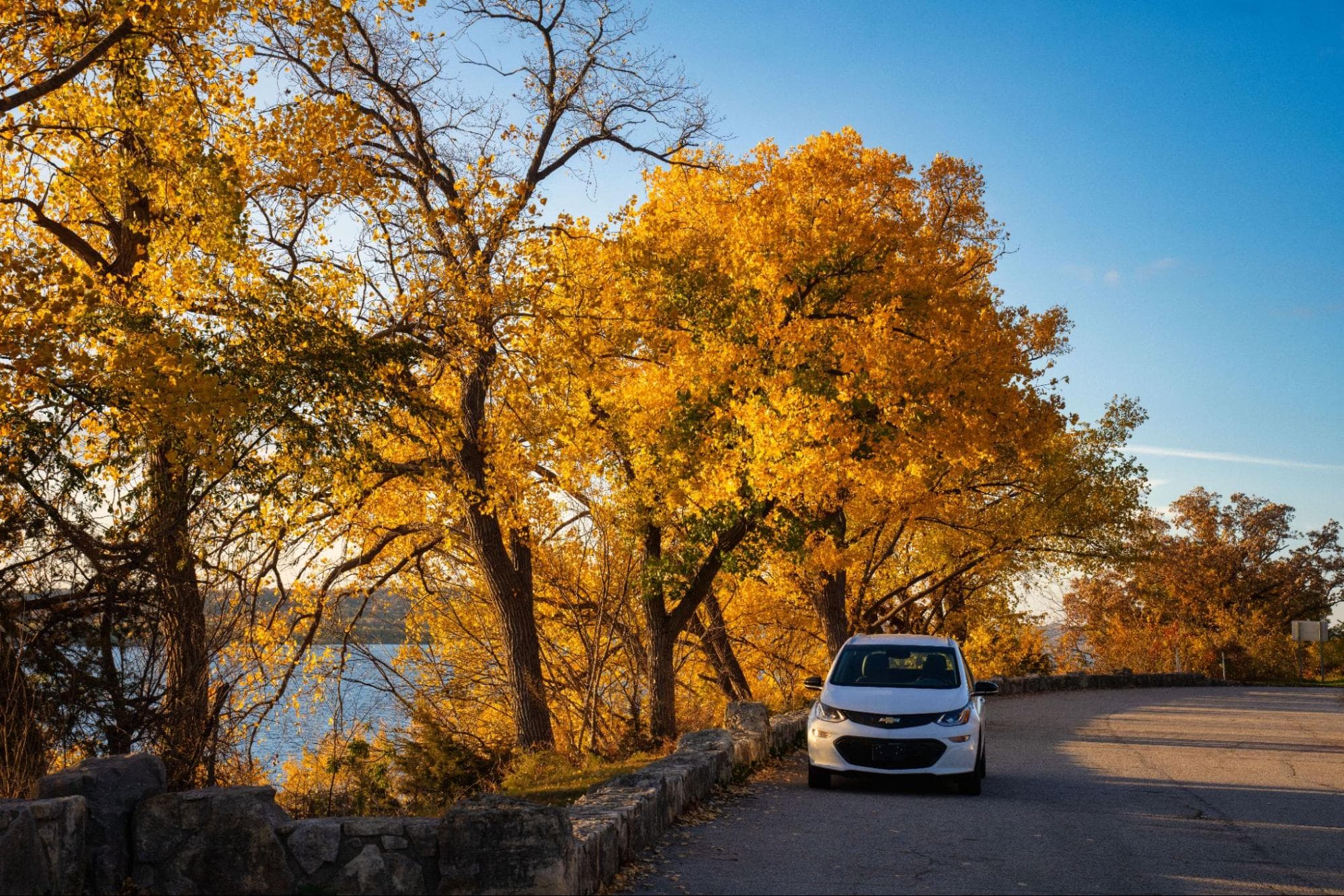 White Chevrolet Bolt on a road in autumn